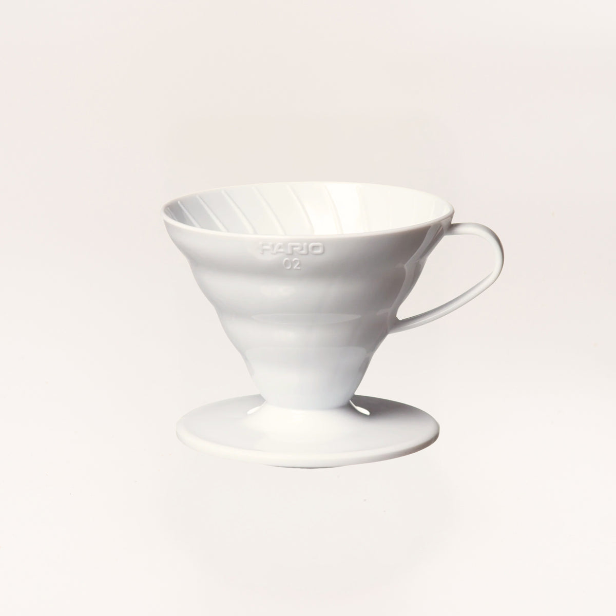 A lightweight white plastic Hario V60 pour-over coffee maker with a matching saucer, photographed against a clean, light off-white background.